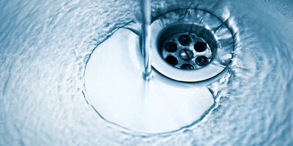 Water flowing down a metal sink drain creating ripples.