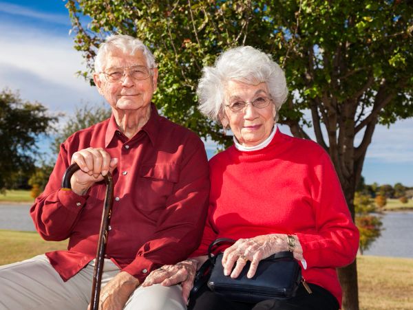 Elderly couple sitting outdoors on a bench, holding hands.