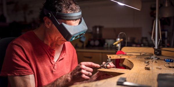 A jeweler carefully files a ring under a magnifying visor in a workshop.