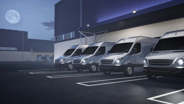 Four silver vans parked in a row outside a building at night.