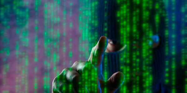 A masked hacker interacts with digital code in a dark environment.