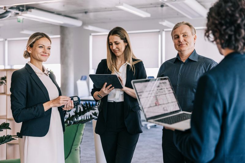 A group of focused financial colleagues engages in a mobile meeting, walking through the office with laptops in hand, exchanging ideas and collaborating effortlessly on the move.
