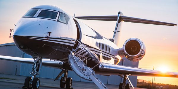Private jet parked on runway with stairs extended at sunset.