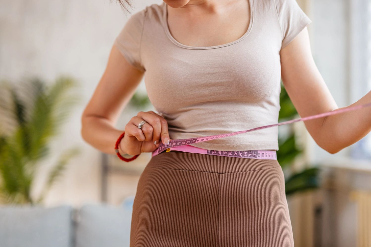 Woman measuring her waist with a pink measuring tape.