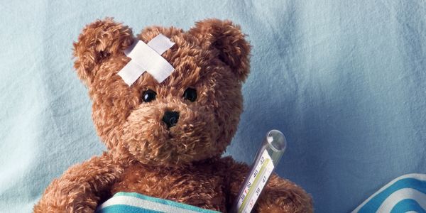 Teddy bear with bandages and thermometer in bed.
