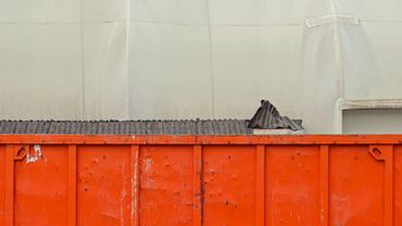 Large orange dumpster in an industrial area with shopping carts behind a fence.