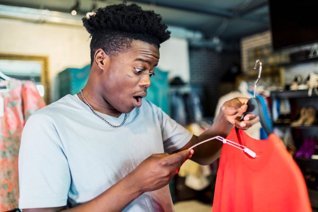 Surprised man looking at price tag on red dress.
