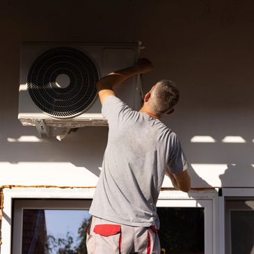 Technician fixing an outdoor air conditioning unit on a sunny day.