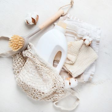 Eco-friendly cleaning essentials including a wooden brush, detergent, and cotton cloths in a mesh bag.