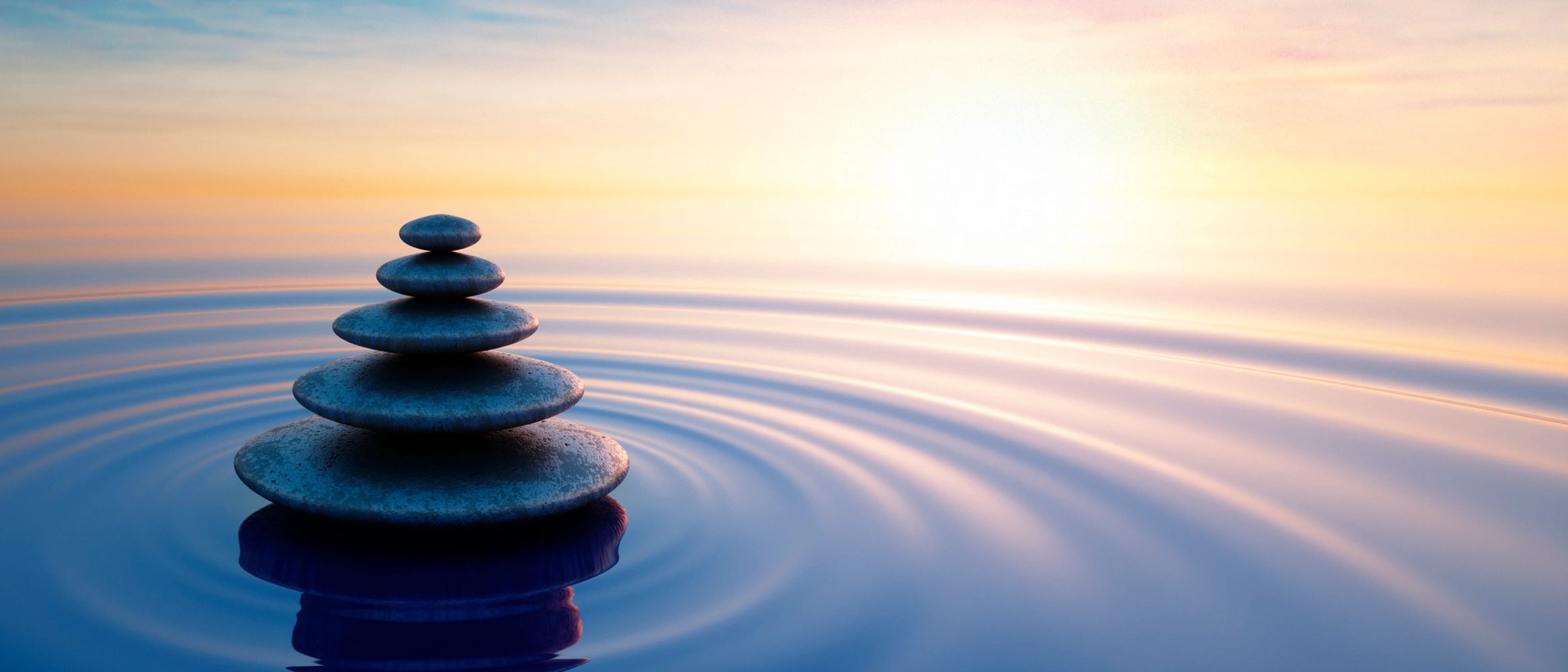 Stacked stones on calm water with sun and ripple reflections.