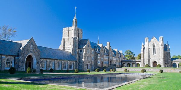 Historic stone building with a reflective pool and manicured lawn under a clear blue sky.