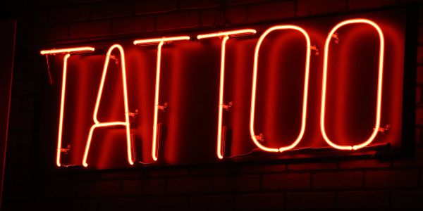 Red neon tattoo sign on a dark brick wall.
