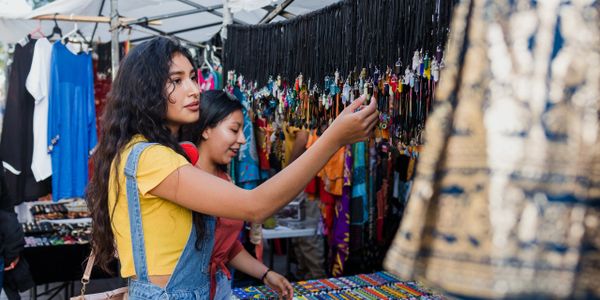 Two women shopping for jewelry at an outdoor market stall.