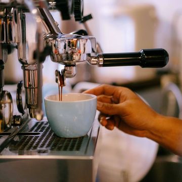 A hand holding a cup as espresso pours from a coffee machine.