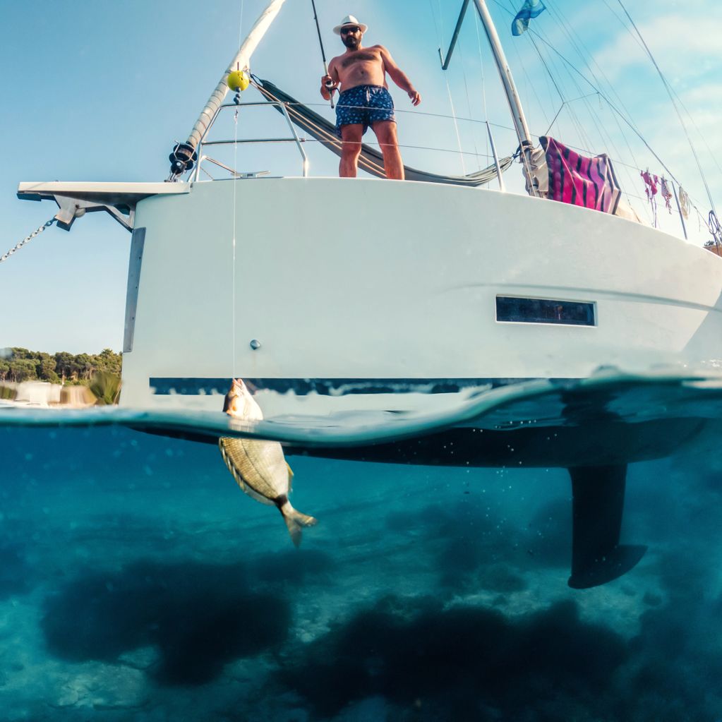 Man fishing from a boat with a fish caught underwater.