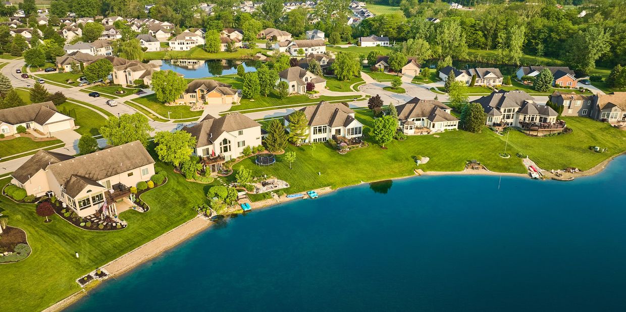 Aerial view of suburban lakeside homes with green lawns and boats.