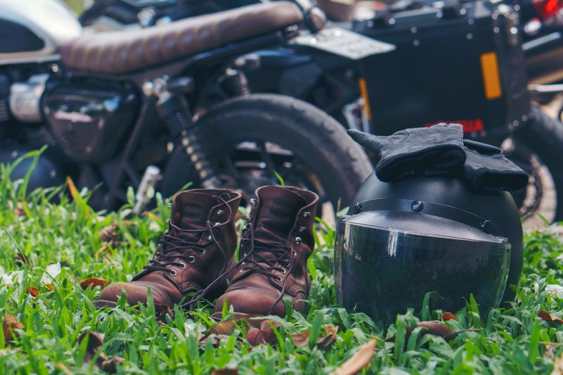 Motorbike parking and biker place helmet, Leather boot, and gloves on green grass. Young Traveller men ride motorcycle on highway, Thailand. Road Trip and lifestyle of motorbike concept.