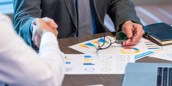 Business handshake over financial documents and charts.