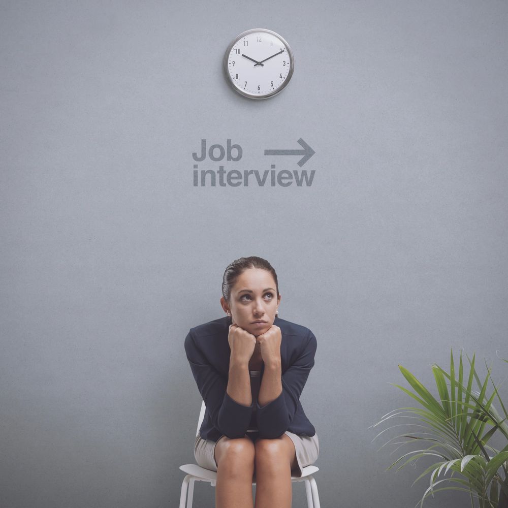 Woman anxiously waiting for a job interview under a clock and sign. she needs career help from legupcareercoaching.com