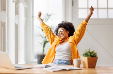 Happy woman stretching at her desk with books and laptop.