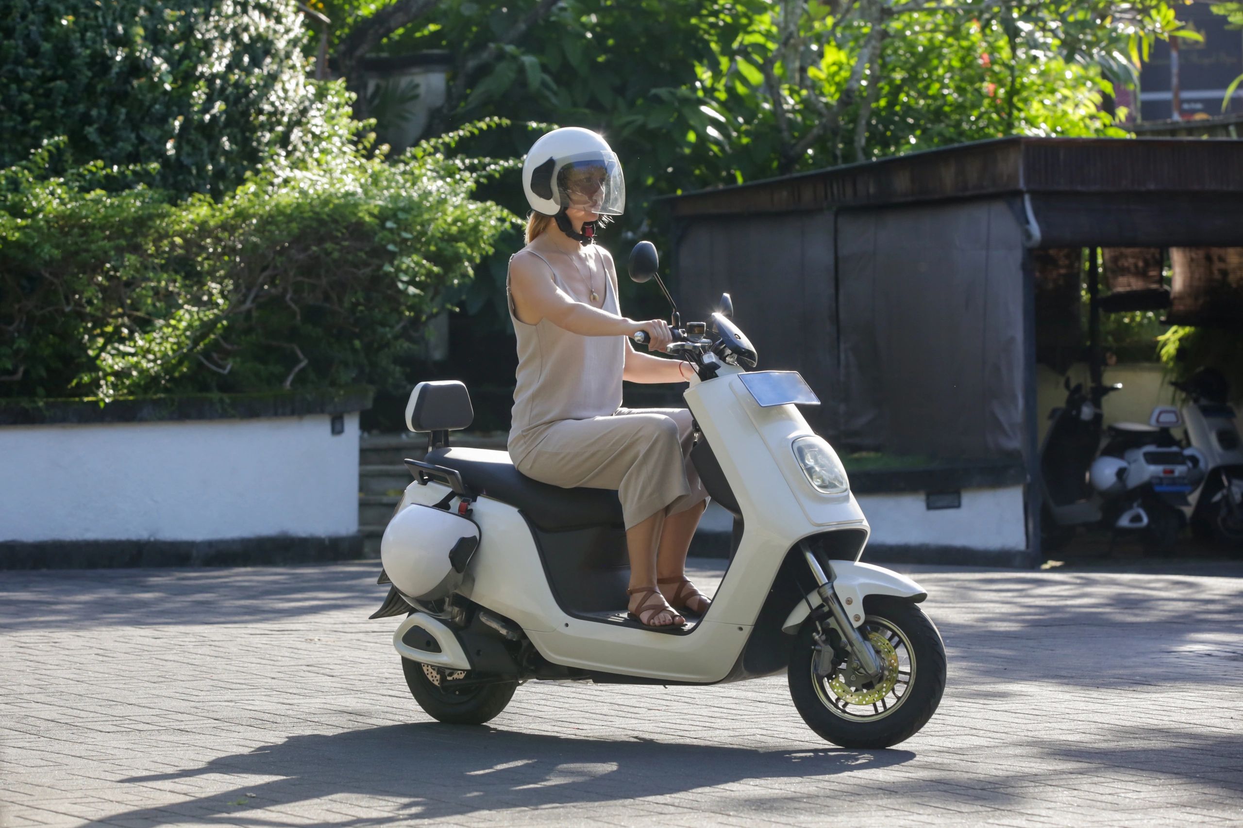 Woman riding a white electric scooter wearing a helmet.
