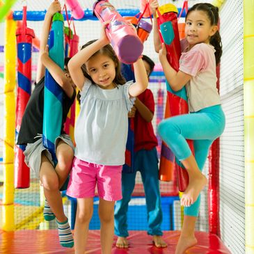 Children playing and climbing on colorful indoor playground equipment.
