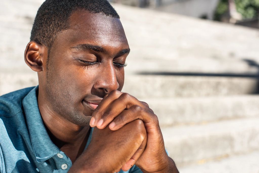Man with eyes closed, hands clasped, appearing to pray.
