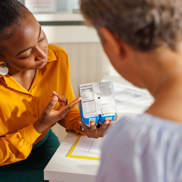 A woman explains nutrition facts on a food package to another person.