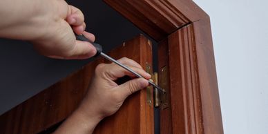 Someone fixing a door hinge with a screwdriver.