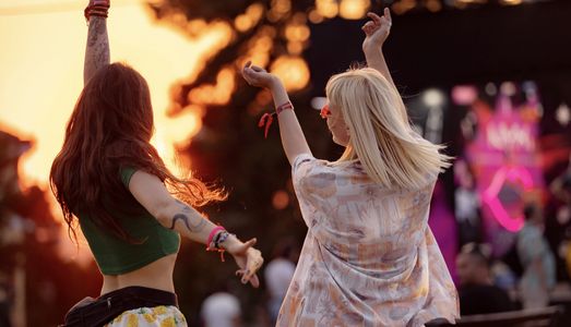 Two women dancing joyfully outdoors at sunset.