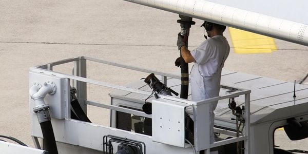 Worker refueling airplane wing at airport with safety gear.
