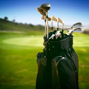 Golf clubs in a bag on a golf course with a clear blue sky.