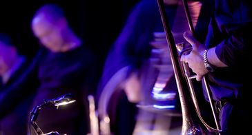 Close-up of a musician playing a trombone under blue stage lighting.