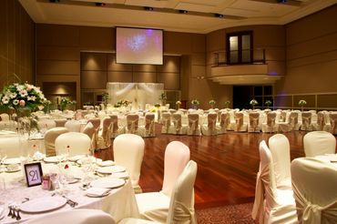 Elegant banquet hall with white-covered chairs and floral centerpieces.