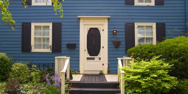 Blue house entrance with white door and lush green bushes.