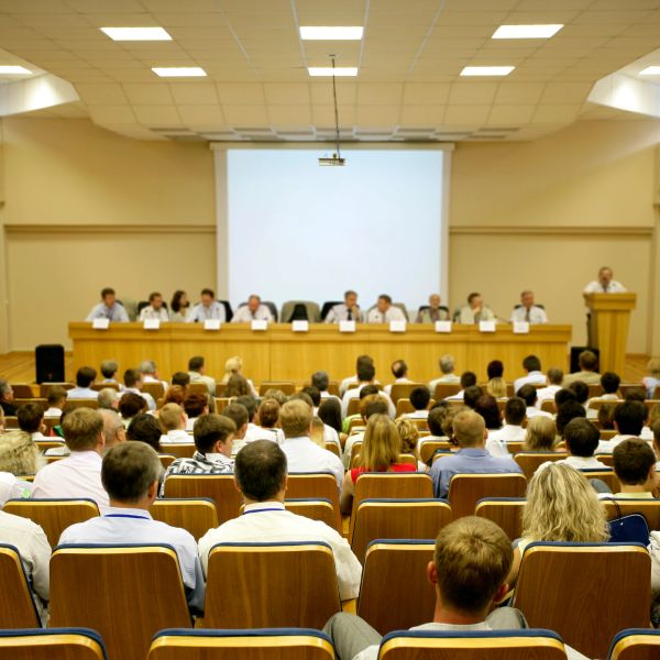 Audience attending a conference with a panel of speakers on stage.