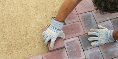 Person placing bricks on sand while wearing work gloves.