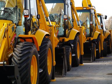 A row of yellow construction backhoe loaders parked closely together.