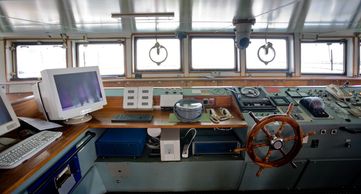 Interior view of a ship's bridge with navigation controls and computer.
