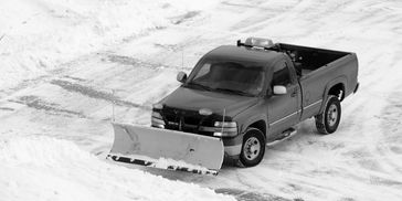A pickup truck equipped with a snowplow clearing snow from a road.