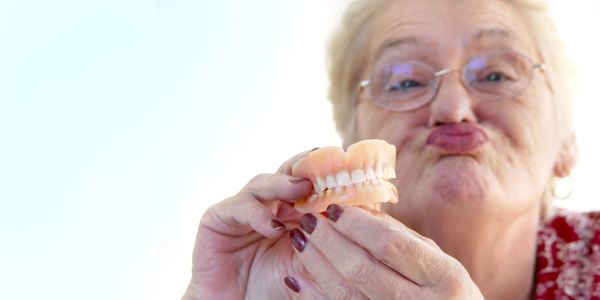 Elderly woman holding dentures and making a playful face.