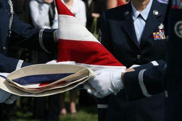 Uniformed personnel folding a U.S. flag with care during a ceremony.