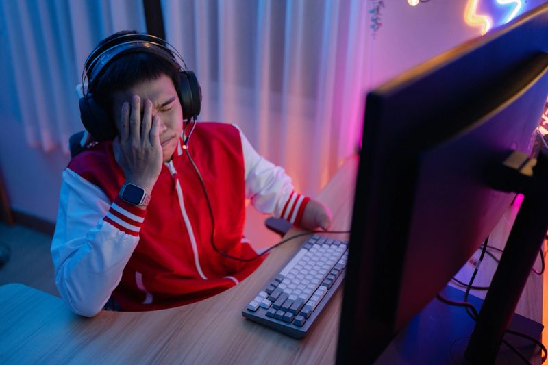 An Asian man in headphones holds a game controller and talks with the team on a microphone during an eSport tournament competition.