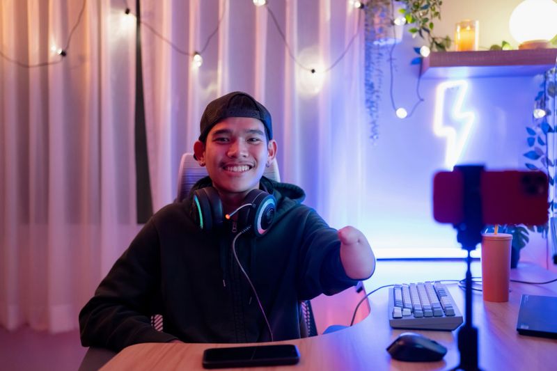 An Asian man in headphones holds a game controller and talks with the team on a microphone during an eSport tournament competition.