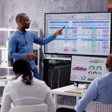 Man presenting financial data on a large screen to colleagues in a modern office.