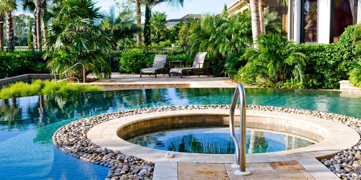 A luxurious backyard pool with a circular hot tub surrounded by palm trees and lounge chairs.