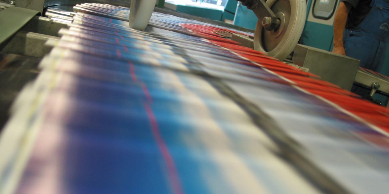 Newspapers being printed rapidly on a printing press.