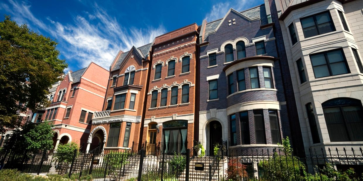 Row of elegant townhouses with varied brick facades under a bright blue sky.