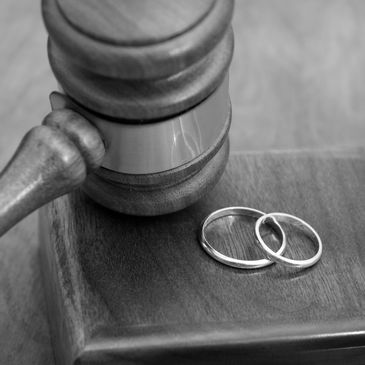 Judicial gavel and two wedding rings on wooden surface.