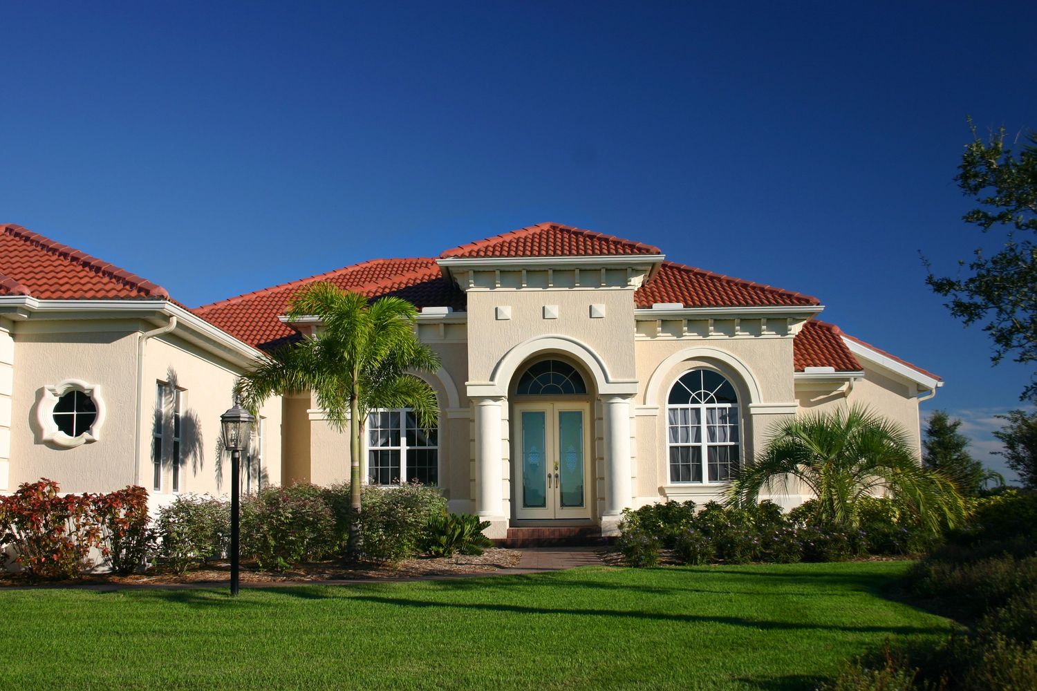 Residential home with stucco exterior, red tile roof, and palm landscaping